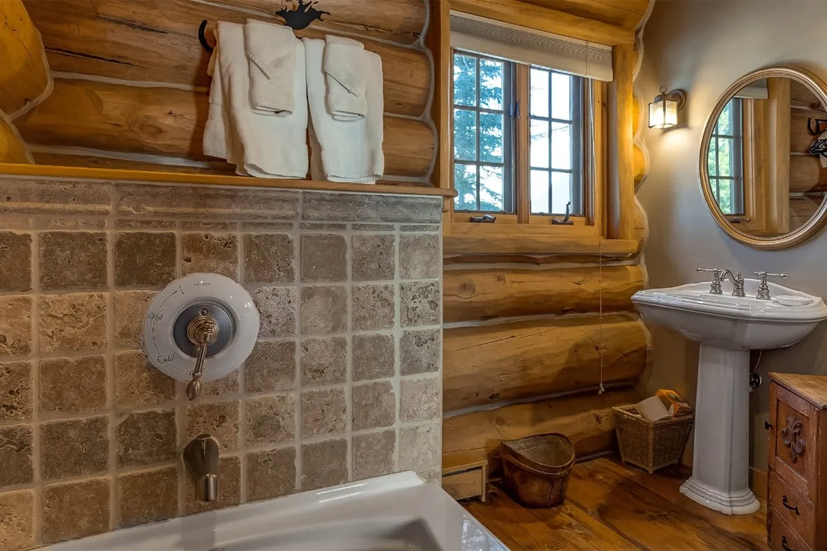 A warm, inviting bathroom with wooden log walls, a vintage-style sink and mirror, and neatly arranged towels. The space suggests self-care and relaxation, ideal for pampering routines after a restful night.