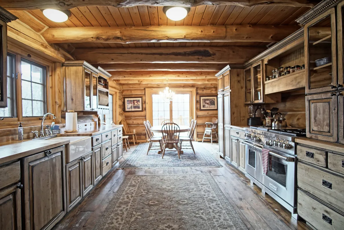 A cozy, well-lit kitchen-dining area showing a kitchen island, adjacent dining table with seating for several, wooden cabinets, and a traditional rug. The layout invites multiple people to participate in both meal preparation and casual dining, reflecting the communal and welcoming atmosphere described in the section.