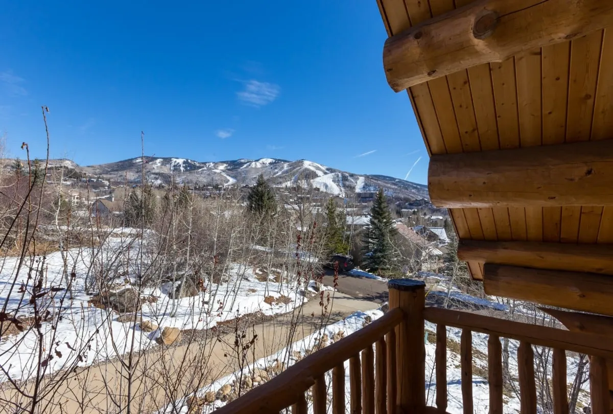 A serene view from a wooden balcony overlooking snow-blanketed ground, trees, and distant mountains. The image emphasizes the property's immediate connection to nature and expansive winter landscapes.