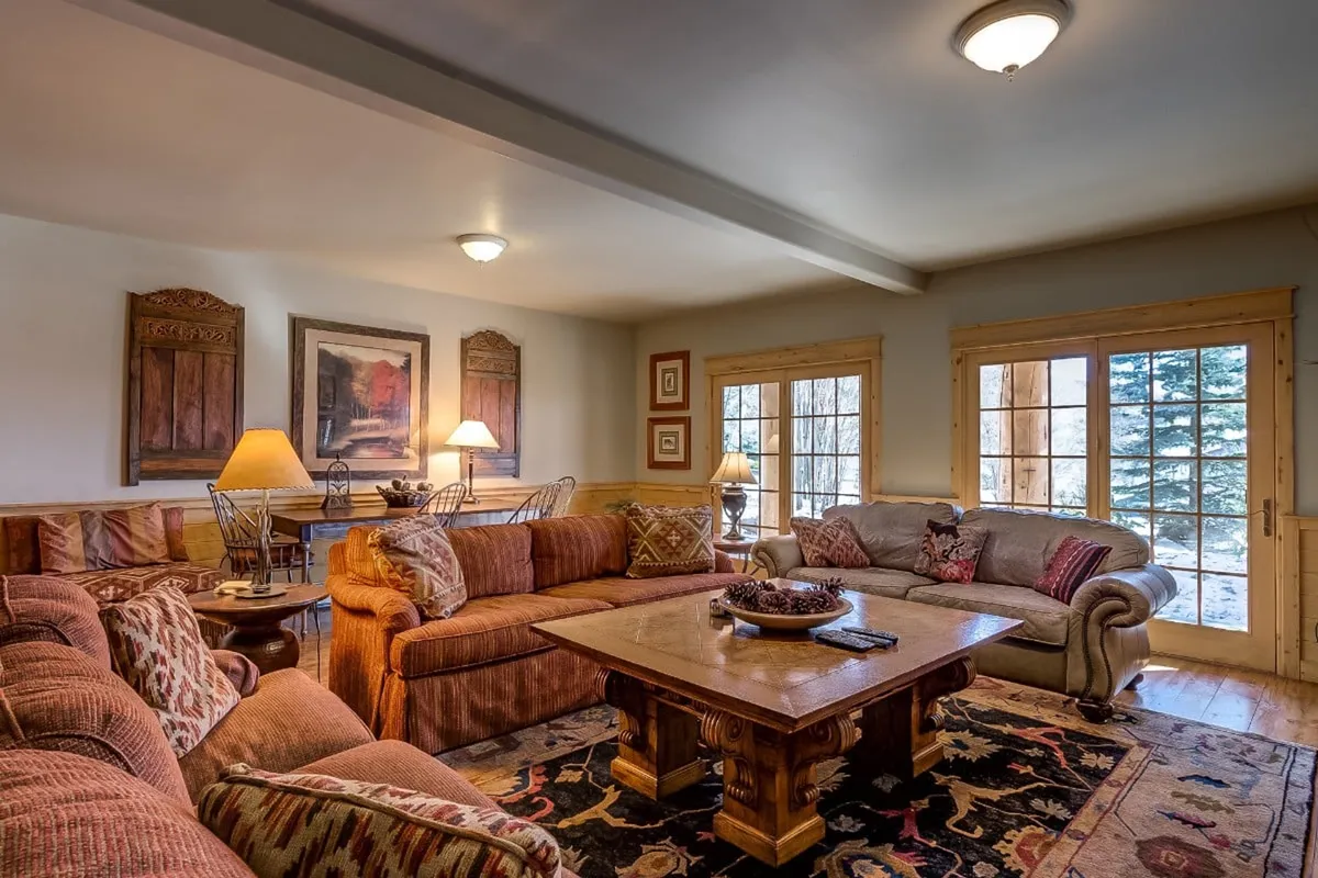 A spacious, welcoming living room with comfortable sofas arranged around a large coffee table, accented by artwork on the walls and expansive windows that draw in daylight. The room exudes warmth and sociability, making it perfect for gathering after a day in town.