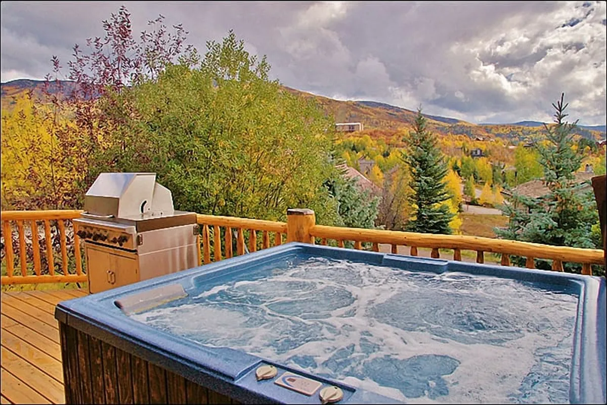 An exterior shot highlighting the hot tub and grill on the deck, framed by mountain views and vibrant fall foliage. The scene captures moments of relaxation, barbecuing, and taking in nature’s beauty—ideal for all-season enjoyment.