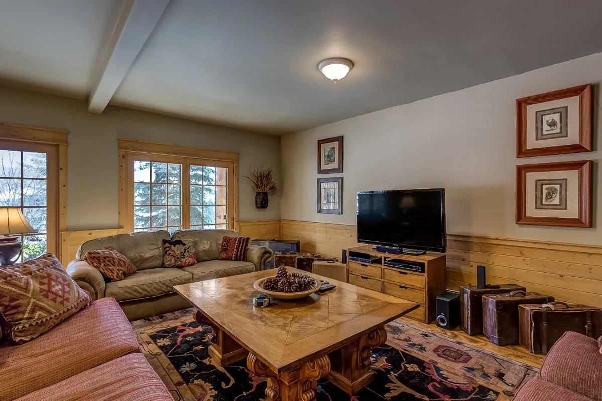 A welcoming interior living space with a large wooden coffee table, comfortable sofas, a television, and framed artwork. The table is perfect for board games or family activities, while the cozy setting hints at evenings spent together after outdoor adventures.
