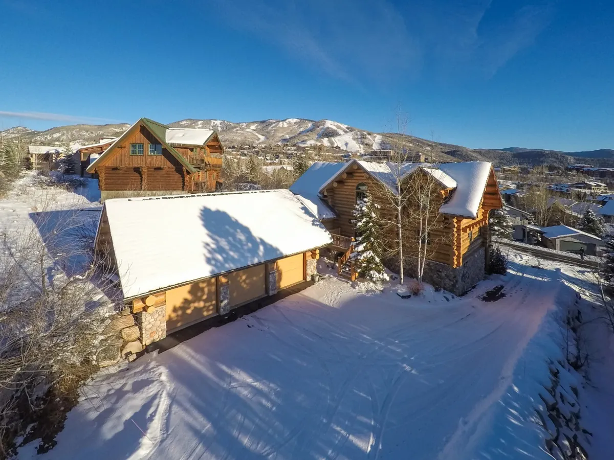 This image showcases the log cabin's classic alpine architecture with snow-covered roofs nestled against a backdrop of surrounding mountains. The scene is quintessentially winter, evoking the thrill of snowy adventures and the cozy retreat awaiting after an active day outdoors.