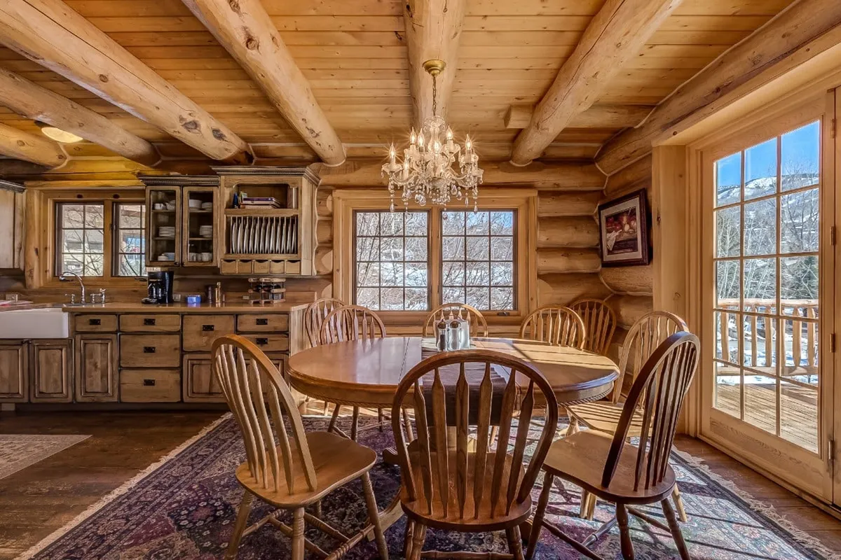 A formal dining area with a large wooden table, elegant chandelier, large windows for natural light, and cabinetry that continues the kitchen's style. The setting is perfect for celebratory feasts or intimate dinners, capturing the spirit of shared meals and special occasions.